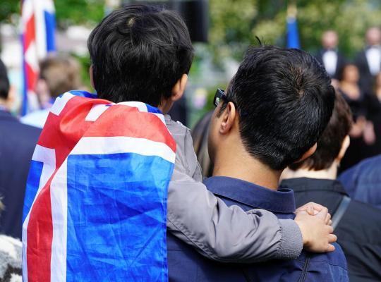 Viewed from behind, a man holding a boy with an Icelandic flag on his back.