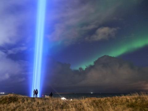 Fólk stendur við Friðarsúluna í Viðey með norðurljós á himni.