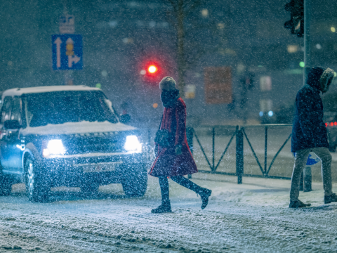 Bíll á götu, snjókoma og fólk.