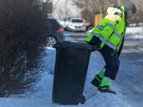 Sorphrðumaður að störfum í snjó með gráa tunnu.