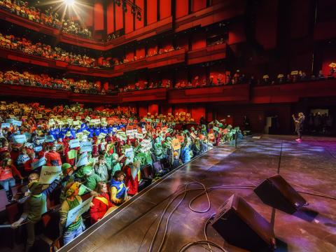 Á opnun Barnamenningarhátíðar 2015 í Eldborg í Hörpu. Sviðið og fullur salur af börnum í litríkum fötum og með skilti sem á stendur t.d. jafnrétti eða ást.
