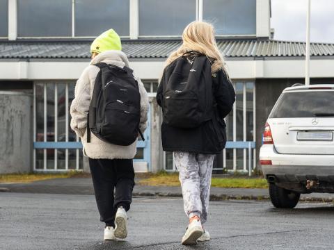 Skólakrakkar að ganga í skólann með skólatöskur á bakinu.