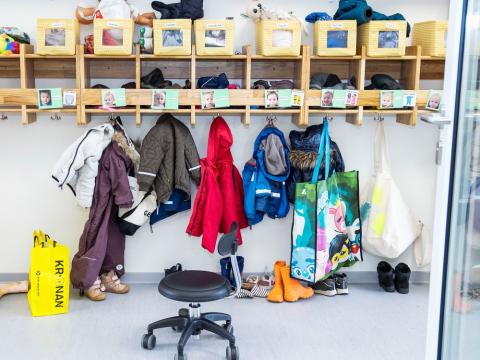 Leikskólaföt hangandi á snögum við hólf barna á leikskóla.