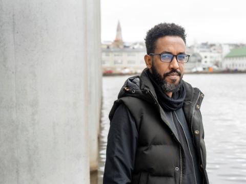 Samson Haileselassie Habte, landflótta blaðamaður frá Erítresu og skjólstæðingur ICORN, stillir sér upp við súlu á Ráðhúsinu. Í bakgrunni er Fríkirkjuvegur og Hallgrímskirkja.