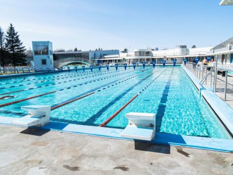 Horft yfir 50 metra laug Laugardalslaugar úti, frá dýpri endanum. Blár himinn.