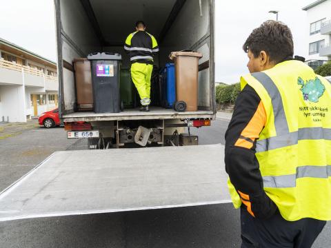 Bíll með sorptunnum og fólk að vinna við tunnuskipti.