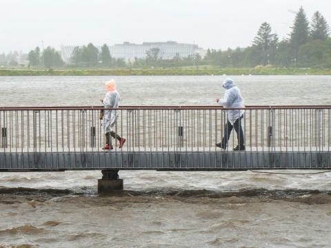 Tvær manneskjur labba á brúnni við Ráðhúsið í roki og rigningu