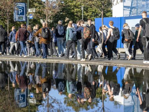 Group of adolescents walking along Tjörnin lake, which reflects their image.