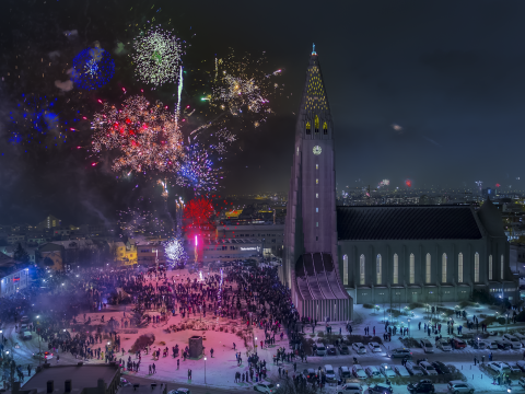 Hallgrímskirkja on New Year's Eve. Church on the right, fireworks exploding, crowds everywhere