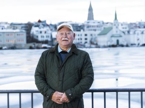 Portrait of Einar D. G. Gunnlaugsson. Standing on the viewing platform by the Tjörnin pond with the pond, Fríkirkja, and Hallgrímskirkja in the background. Winter, ice.