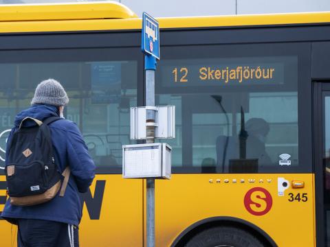 maður sem stendur fyrir utan strætisvagn, strætóskilti til hliðar.