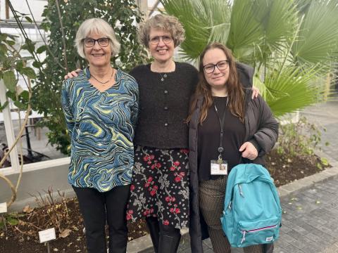 Þrjár konur með plöntur í baksýn.