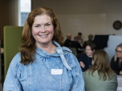 Kona að brossa með fólk í baksýn.