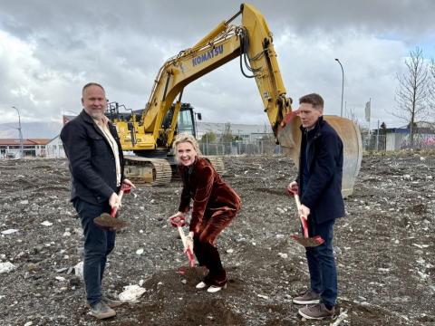 Two men and one woman break ground with an excavator in the background