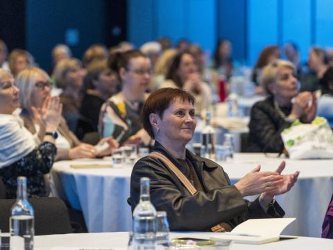 A woman sits in the front of a group and applauds one of the presentations at Licensed Practical Nurse Day. 