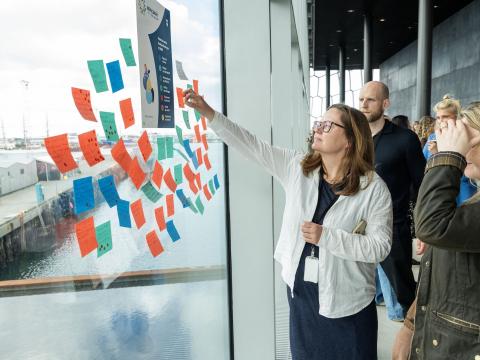 A woman places Post-it notes on a window at Harpa, which is how ideas were collected for Reykjavík City's new Welfare Policy action plan