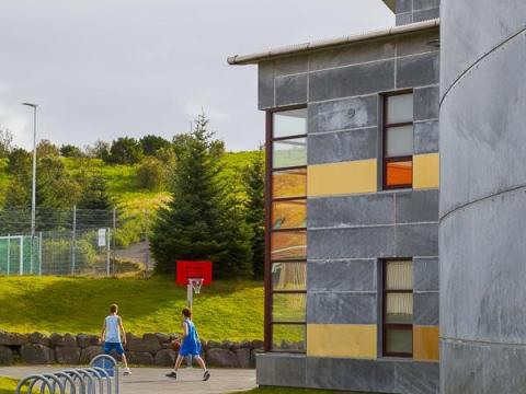 Photo of Húsaskóli. Two children play basketball on a playground.