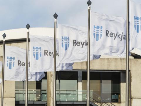 Nærmynd af Reykjavíkurfánum á brúnni við Tjörnina, fánarnir sjálfir og sést í Ráðhúsið í bakgrunni.