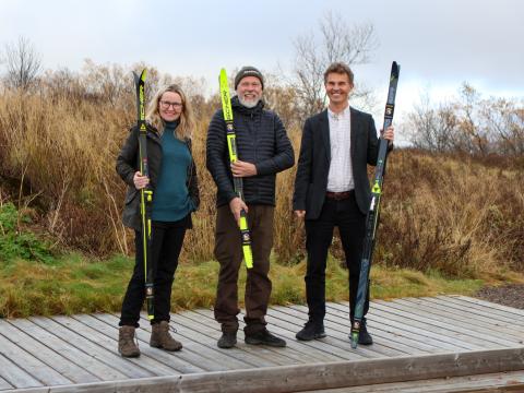 Ásta Briem, executive director of Icebike Adventures, Magne Kvam, cross-country trail designer, and Skúli Helgason, chair of Reykjavík's Culture and Sports Council, posed for a photo after signing the ski trail agreement at Rauðavatn. Posing with cross-country skis surrounded by vegetation.