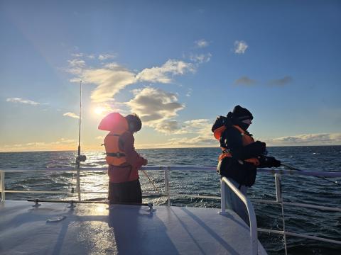 Two kids in life jackets with fishing rods while fishing out at sea.