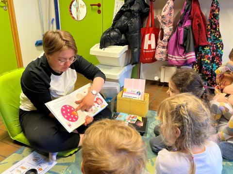 Photo of a preschool staff member showing pictures in a book to children.