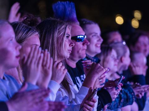 Close-up of people in the front row at a concert. Dark, people of all ages.