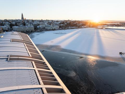 Þak Ráðhússins í forgrunni, ísilögð Tjörn, sólin að koma upp í fjarska. Hallgrímskirkja og Þingholtin í bakgrunni.