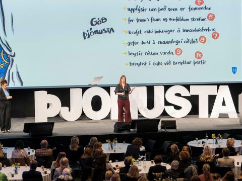 Arna Ýr Sævarsdóttir, skrifstofustjóri þjónustu og umbreytinga á þjónustu- og nýsköpunarsviði, á stjórnendadegi Reykjavíkurborgar í Hörpu 2024. Arna fyrir miðju sviði, stafirnir ÞJÓNUSTA áberandi á sviðinu, glærur á bakvið. Sitjandi gestir í forgrunni.