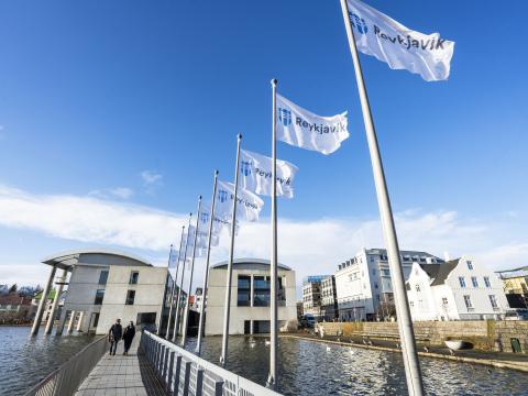Ráðhús Reykjavíkur, horft frá enda brúarinnar. Reykjavíkurfána flaggað á fánaröð brúar. Blár himinn.