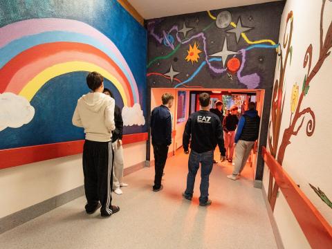 Séð aftan á ungmenni á gangi skóla, kringum þau eru litríkir veggir, til dæmis regnbogi málaður á einn vegginn.