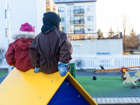Children sitting on a small playhouse in a preschool yard.