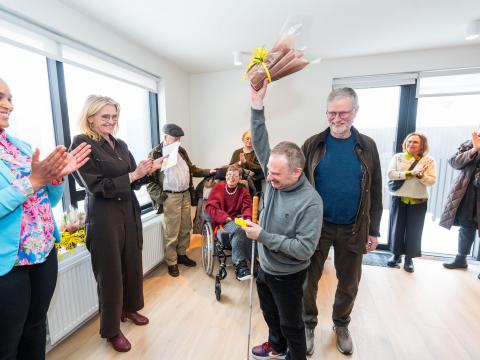 Kjartan Ásmundsson lyftir blómum upp í loft eins og bikar til að fagna því að hafa fengið lykla að íbúð sinni. Á myndinni eru líka borgarstjóri og formaður velferðarráðs. 