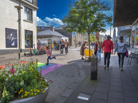 Fólk á gangi, blóm og tré.