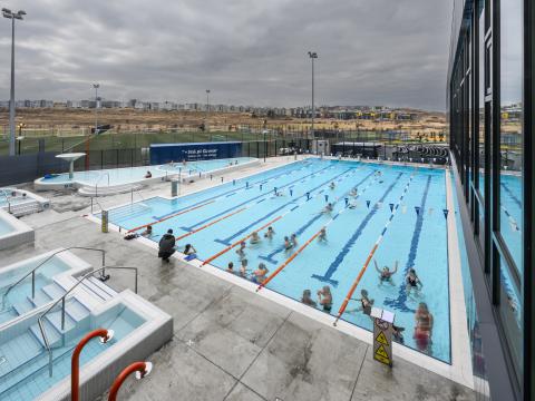 Dalslaug, mynd tekin niður á við yfir sundlaugasvæðið, frá húsinu. Fólk í lauginni. Skýjað úti.