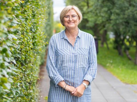 Vilhelmína Þ. Einarsdóttir stendur við trérunna með bros á vör