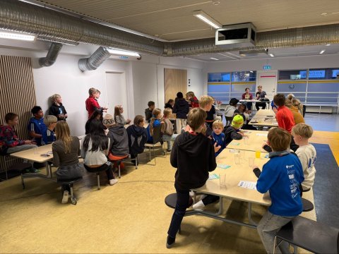 Börn sitja við tvö stór langborð.