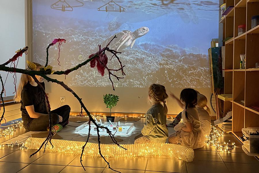 Kennari og krakkar horfa á dýralífsmynd inni á leikskólanum Jörfa.