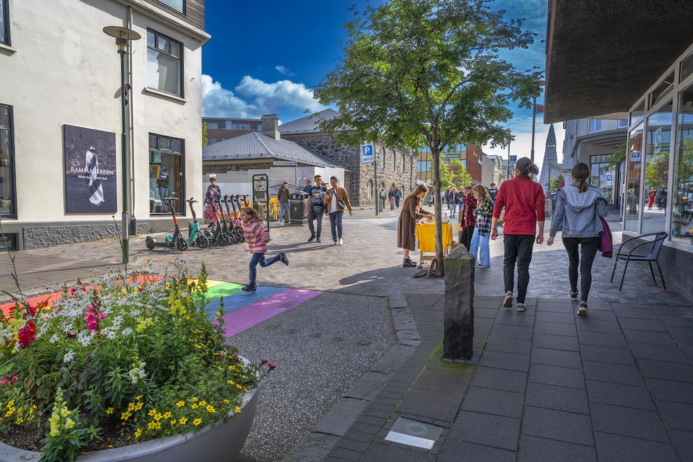 Fólk á gangi, blóm og tré.