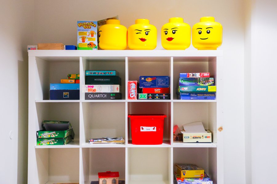 Shelf containing various board games with large Lego figure heads displayed on the top shelf.