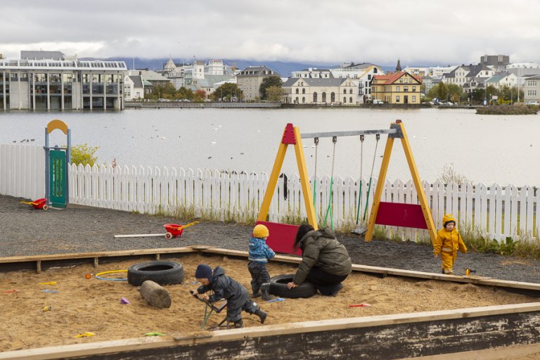 Börn í sandkassa með rólur í baksýn á útisvæði leikskólans Tjarnar