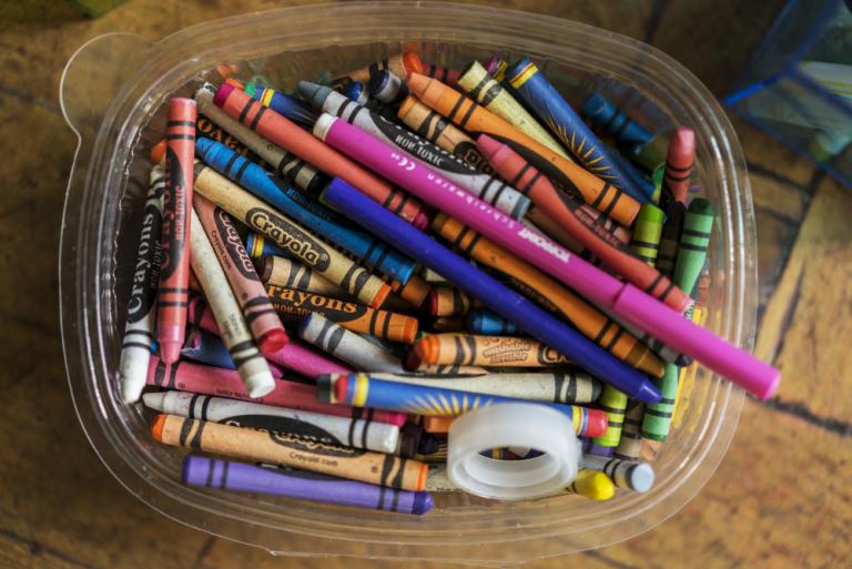 Vaxlitir, tveir tússlitir og límbandsrúlla í plastboxi, loftmynd.