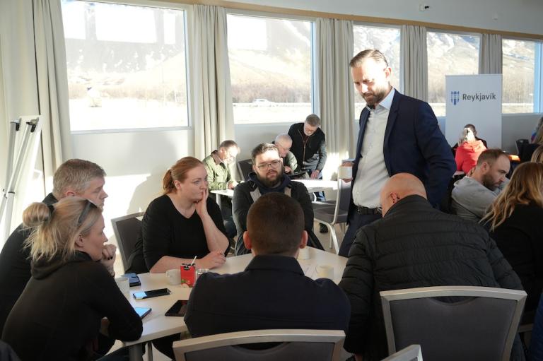 Einar Þorsteinsson spjallar við fólk á fundi og sólríkur dagur sést í gegnum glugga