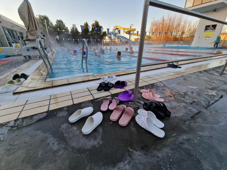 Skór sundgesta við Breiðholtslaug, eldri borgarar í sundleikfimi í baksýn