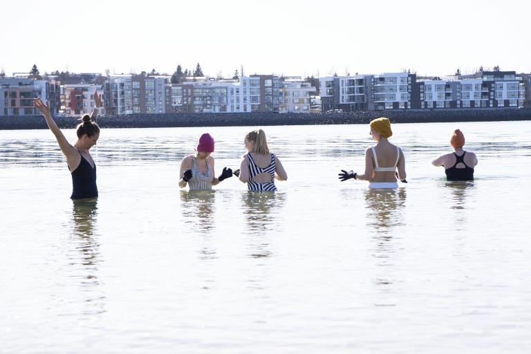 Fimm konur í sjónum í Nauthólsvík. Vetur en fallegt veður og sjórinn sléttur.