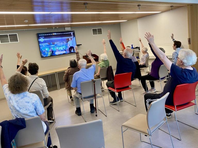 Séð aftan á hóp fólks gera æfingar með fjarþjálfara. 