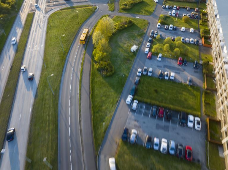 Aerial photo of a Strætó Public Transport bus driving on a street surrounded by greenery. A parking lot is visible on the right.