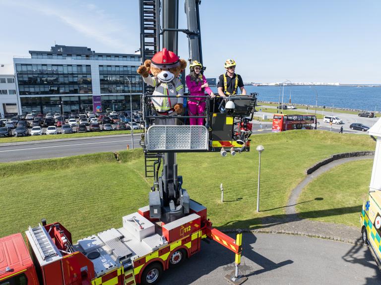 Fire safety bear Bjørnis, Mayor Heiða Björg and firefighter in the basket of an aerial platform truck, high above Höfði. Advania in the background.