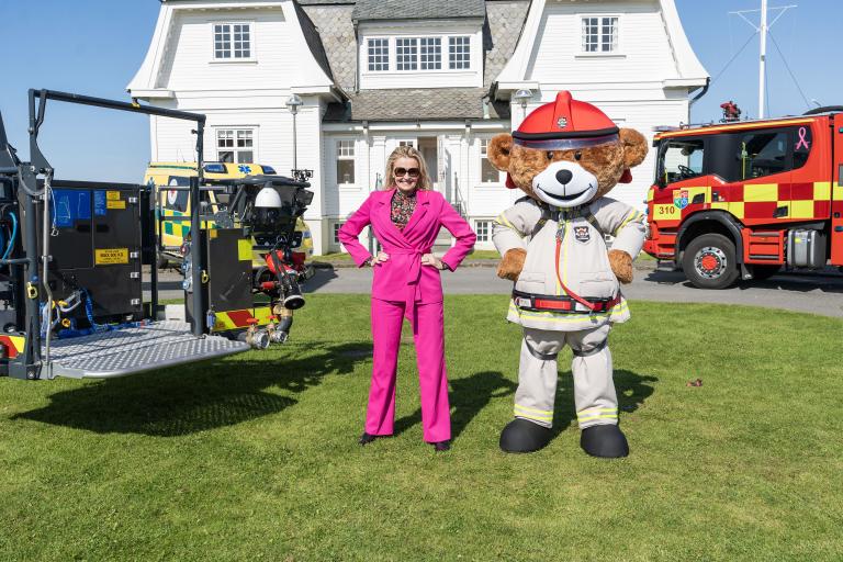 Mayor Heiða Björg Hilmisdóttir and fire safety bear Bjørnis posed outside Höfði in pleasant weather. Fire truck and Höfði in the background.