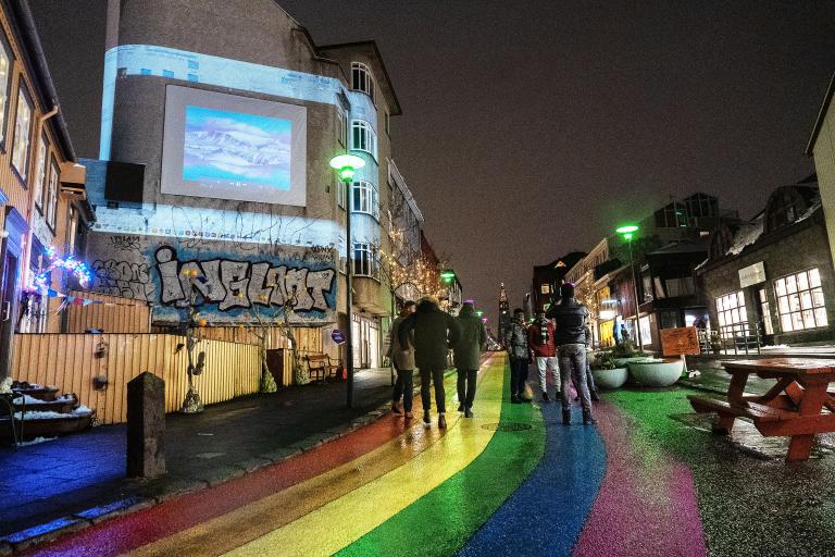 Artwork at the 2023 Winter Lights Festival. Image projected on a wall at the bottom of Skólavörðustígur, looking toward Hallgrímskirkja along the rainbow street. Darkness, people walking.