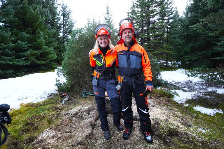 Mayor Heiða B. Hilmisdóttir was assisted by Sævar Hreiðarsson, a forest ranger with the Reykjavík Forestry Association, to fell the 2025 Oslo tree. They stand together by the freshly felled tree, wearing safety gear and helmets.